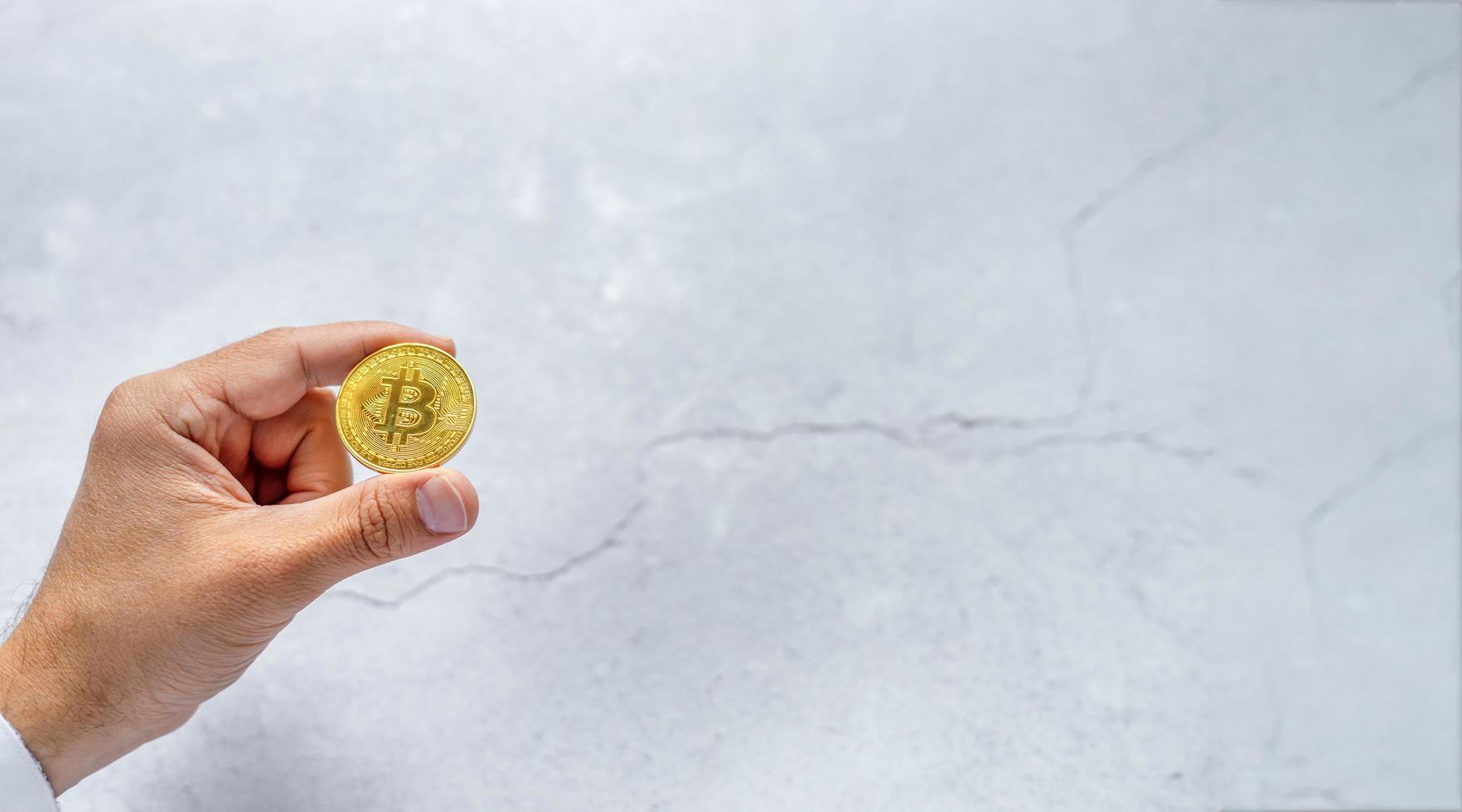 crypto uitwisseling 2022. bitcoin geld. een hand- Holding een gouden munt, Aan een grijs achtergrond. banier met ruimte voor tekst foto