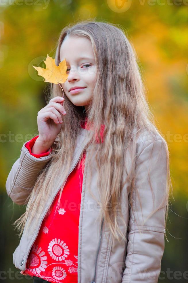 aanbiddelijk weinig meisje met herfst bladeren in de mooi park foto