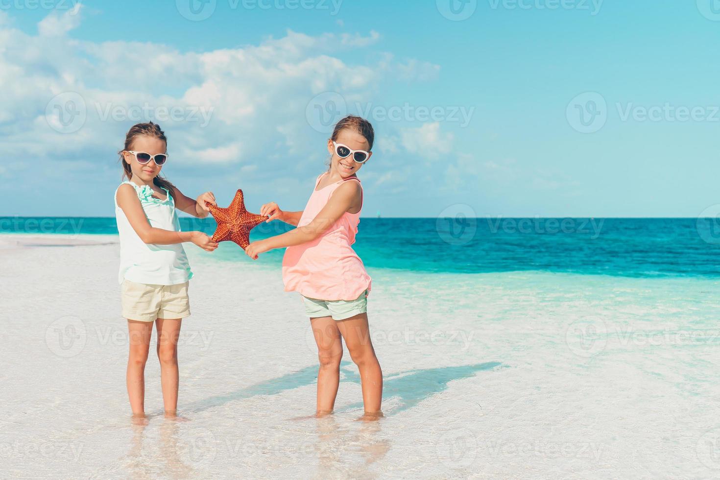 aanbiddelijk weinig meisjes met zeesterren Aan wit leeg strand foto