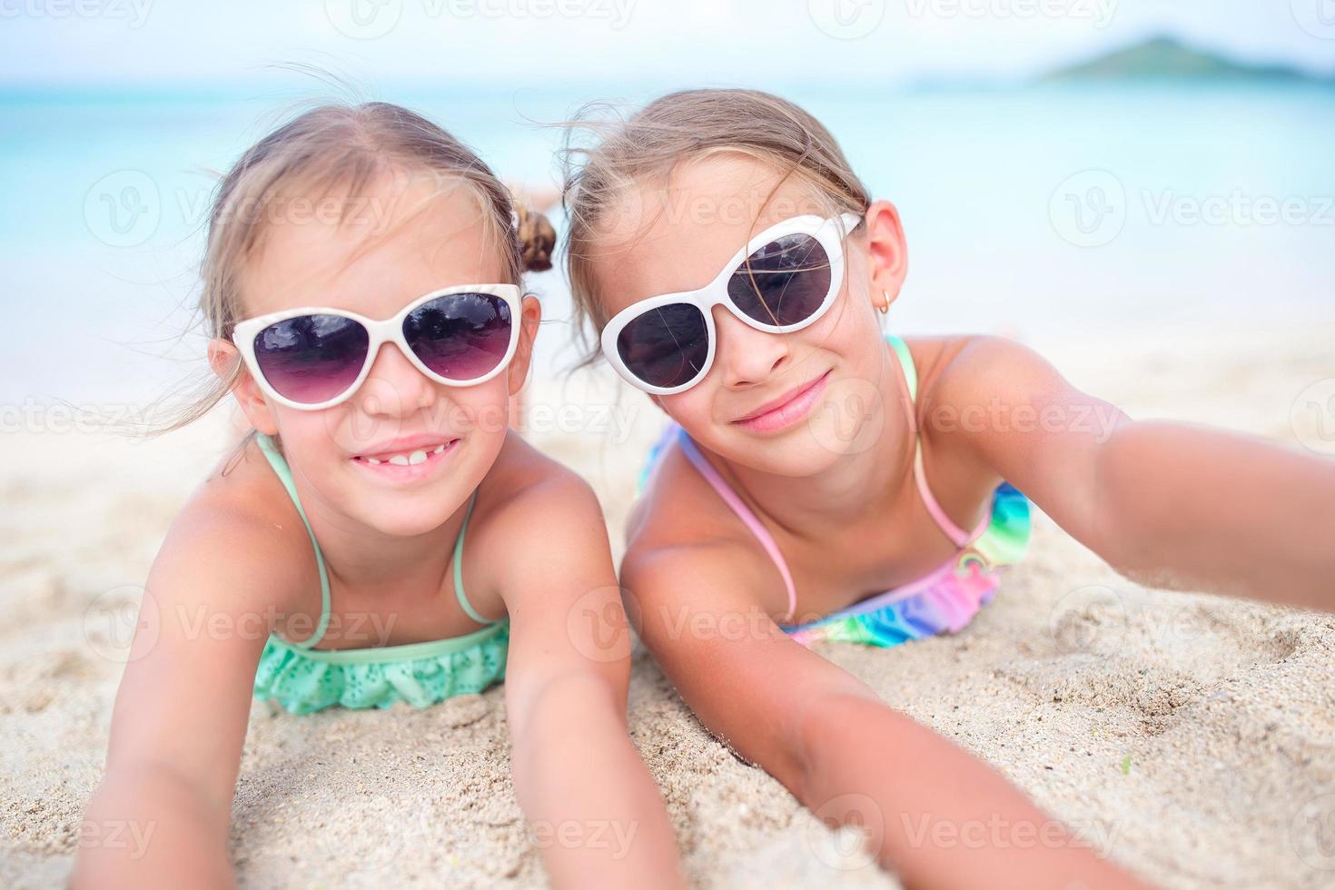 dichtbij omhoog weinig meisjes Aan zanderig strand. gelukkig kinderen aan het liegen Aan warm wit zanderig strand foto