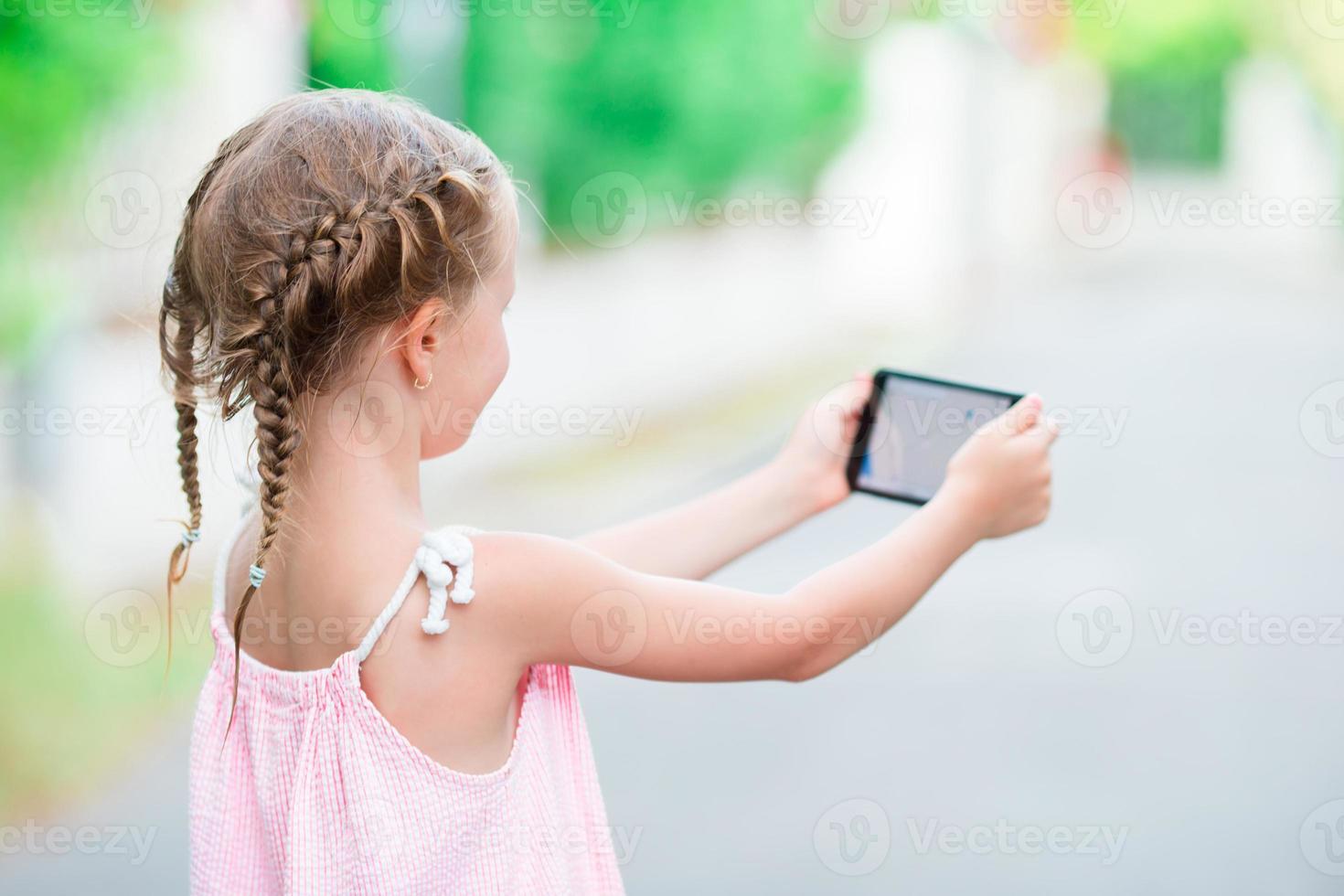 aanbiddelijk weinig meisje met telefoon gedurende zomer vakantie buitenshuis foto