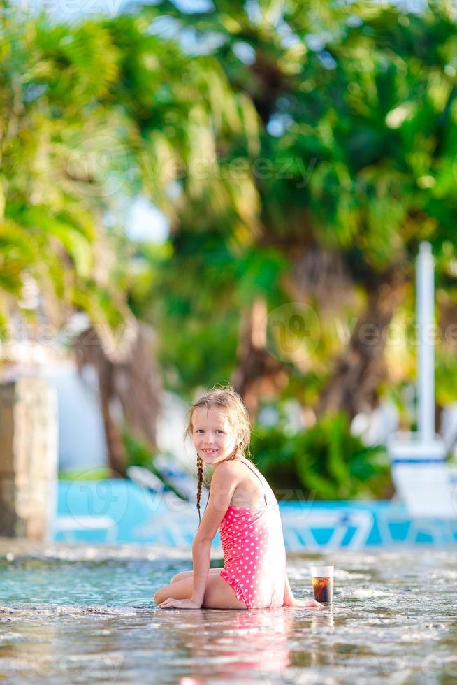 weinig meisje in buitenshuis zwemmen zwembad genieten haar vakantie met smakelijk drinken foto