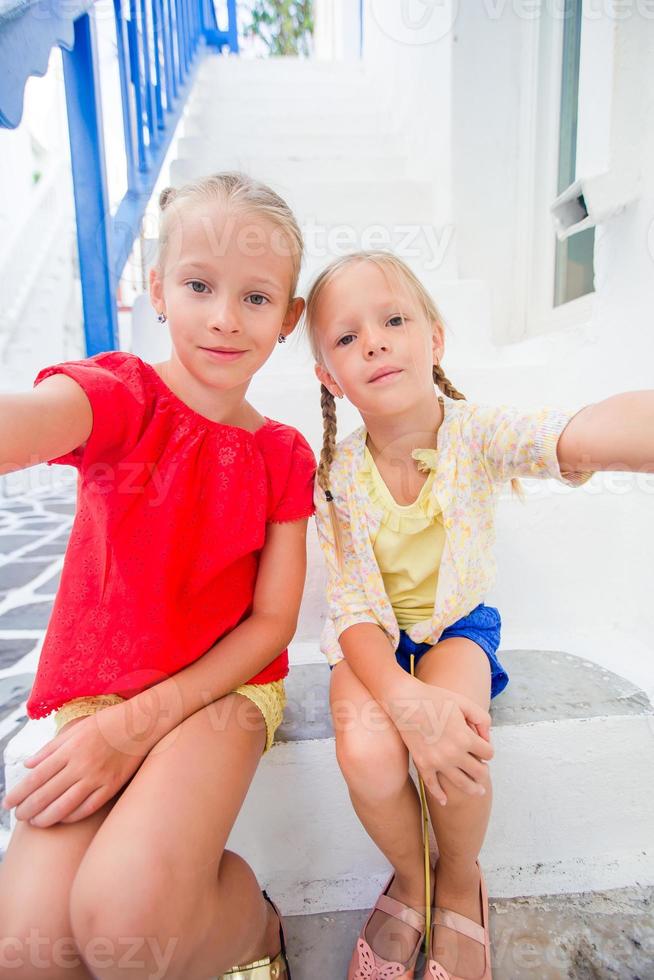 twee meisjes in blauw jurken hebben pret buitenshuis Aan Mykonos straten foto