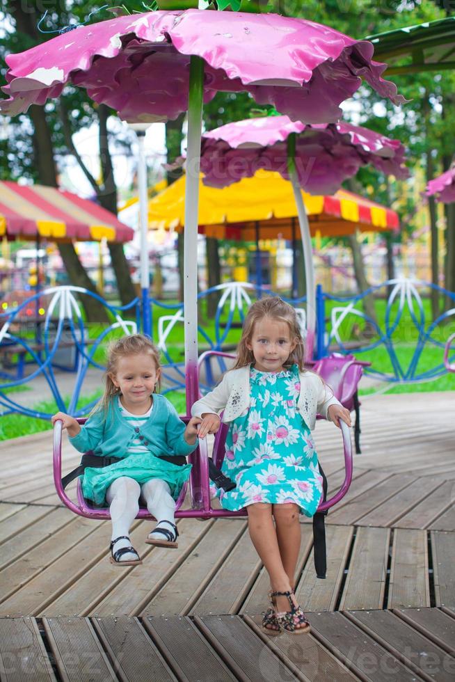 twee weinig mode lief zussen rijden Aan de carrousel in de park foto