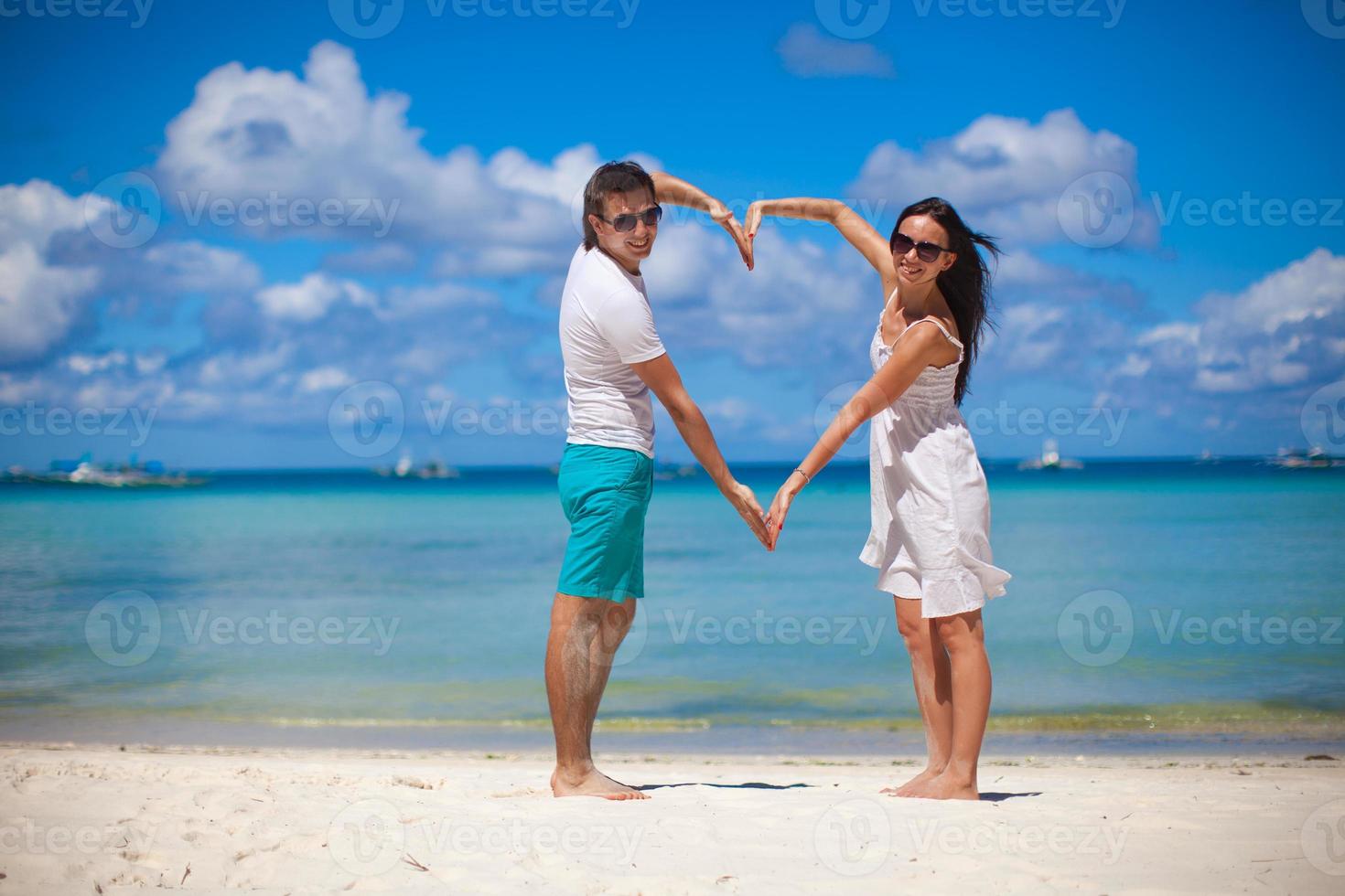 jong paar genieten van elk andere Aan een tropisch strand en maken hart met handen foto