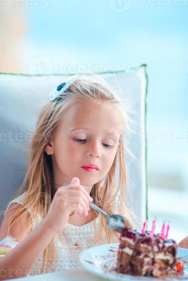 weinig meisje vieren gelukkig verjaardag met smakelijk taart in buitenshuis cafe foto