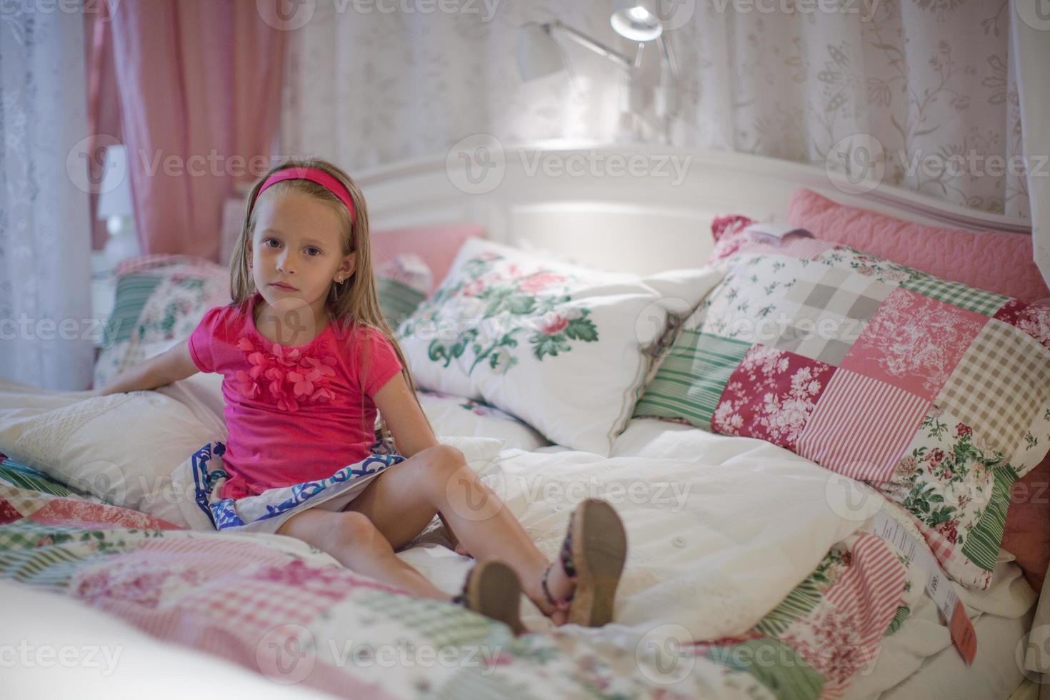 weinig meisje zittend in een groot kleurrijk bed foto