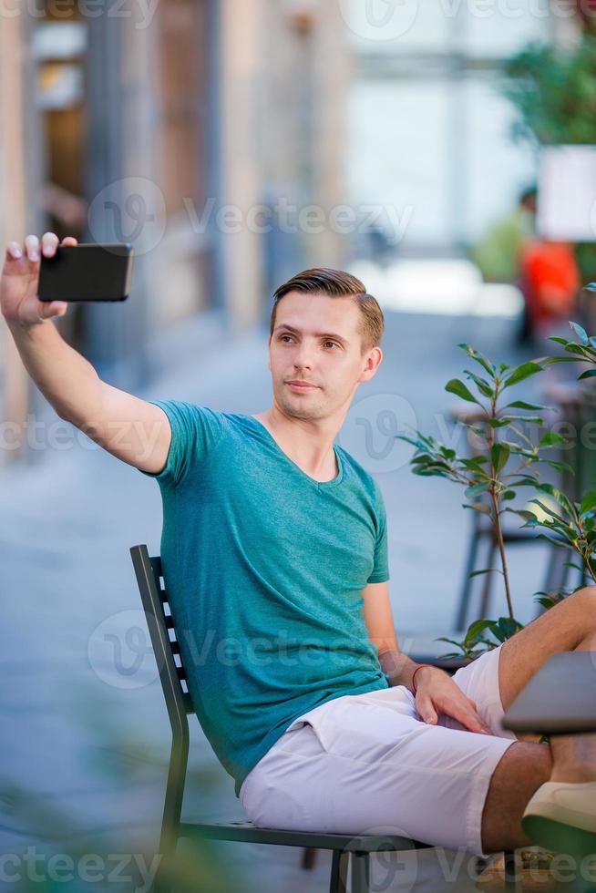 Kaukasisch toerist met smartphone nemen selfie zittend in buitenshuis cafe. foto