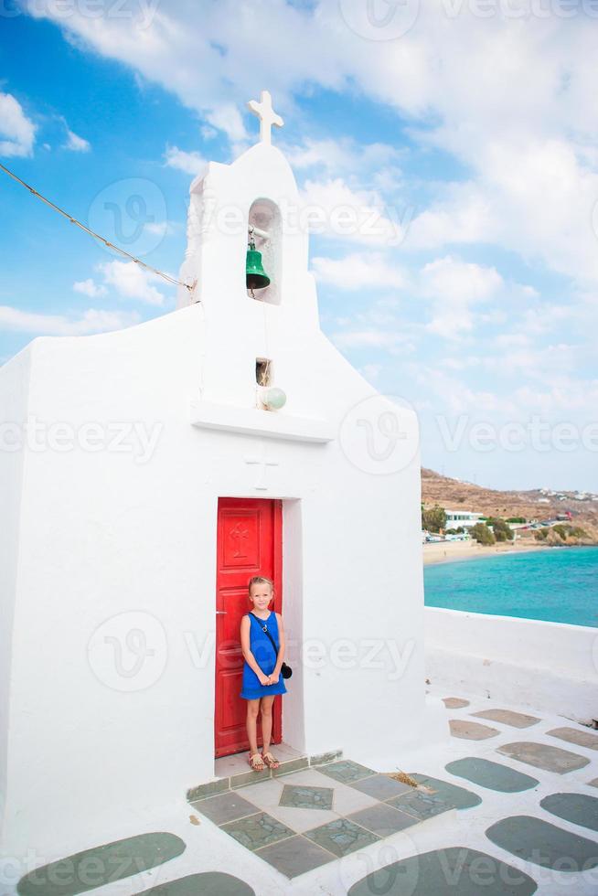 schattig meisje in blauw jurk buitenshuis in de buurt kerk. kind Bij straat van typisch Grieks traditioneel dorp Aan Mykonos eiland foto