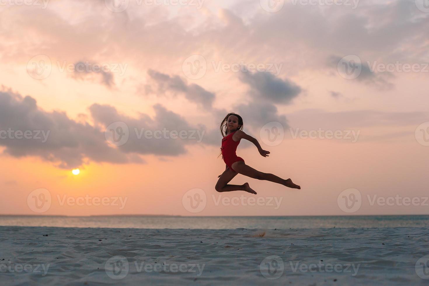 aanbiddelijk gelukkig weinig meisje Aan wit strand Bij zonsondergang. foto