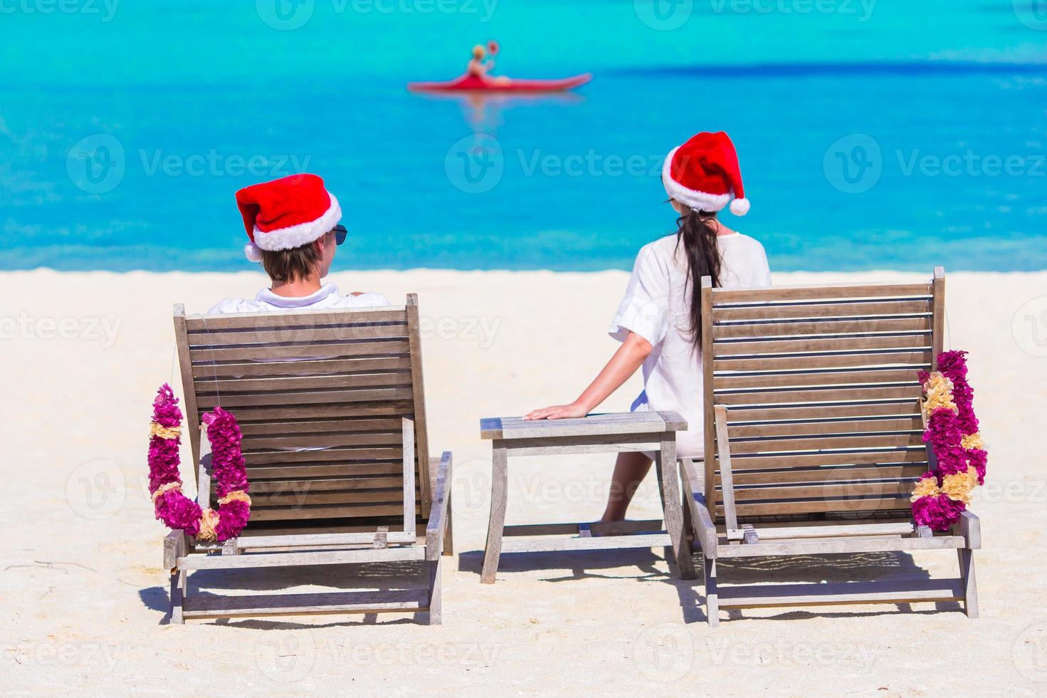 jong paar in de kerstman hoeden ontspannende Aan strand gedurende Kerstmis vakantie foto