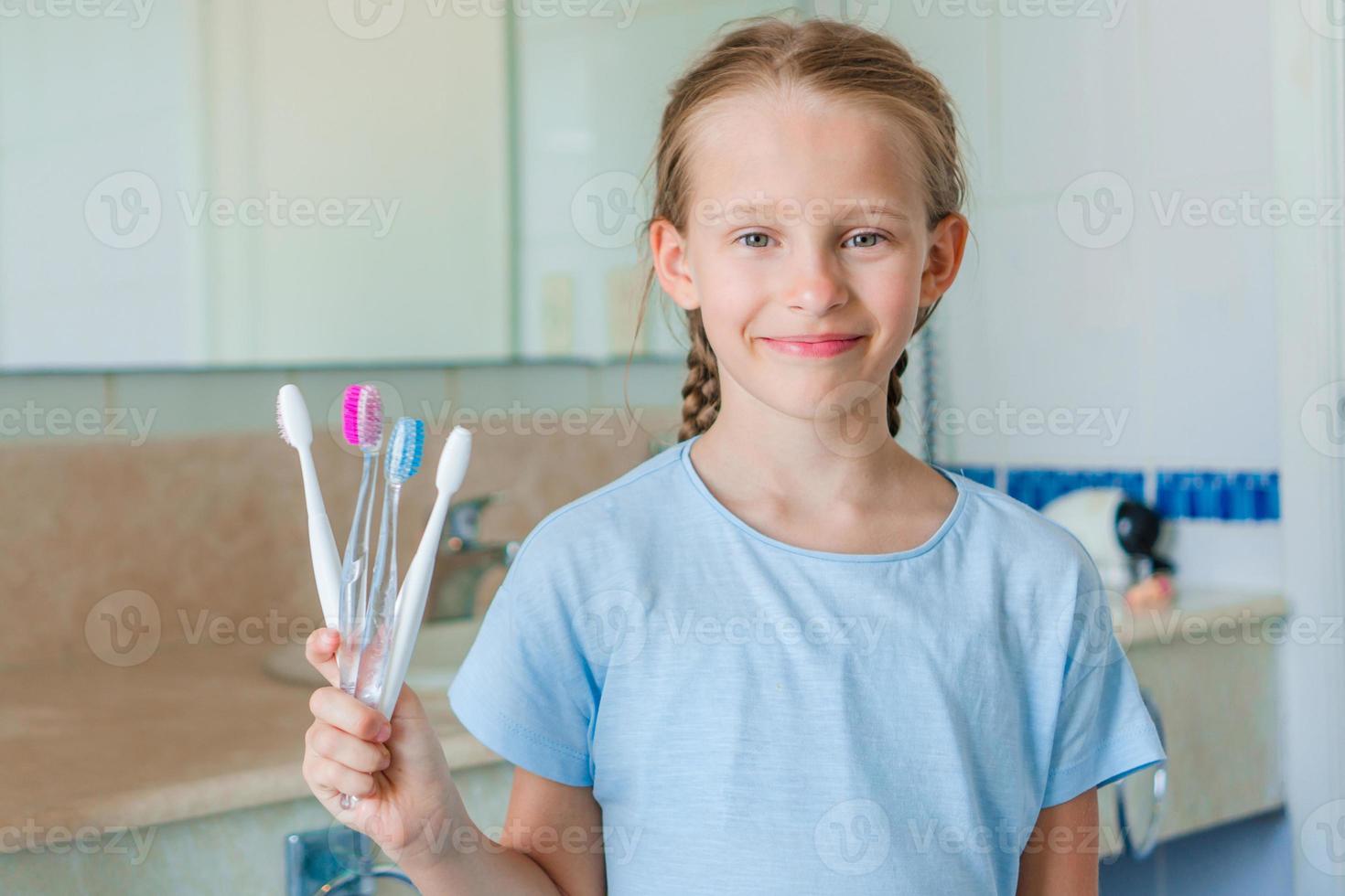 weinig mooi meisje met wit tanden met tandenborstels in handen in de badkamer foto