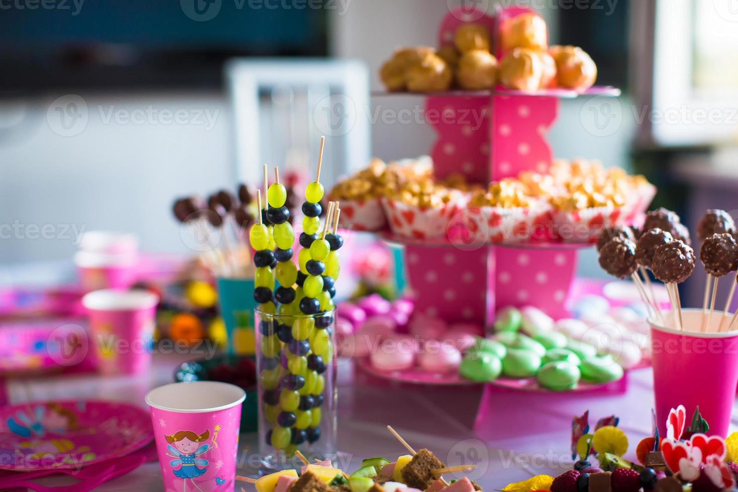 canapé van fruit, wit chocola taart knalt en popcorn Aan zoet kinderen tafel Bij verjaardag partij foto