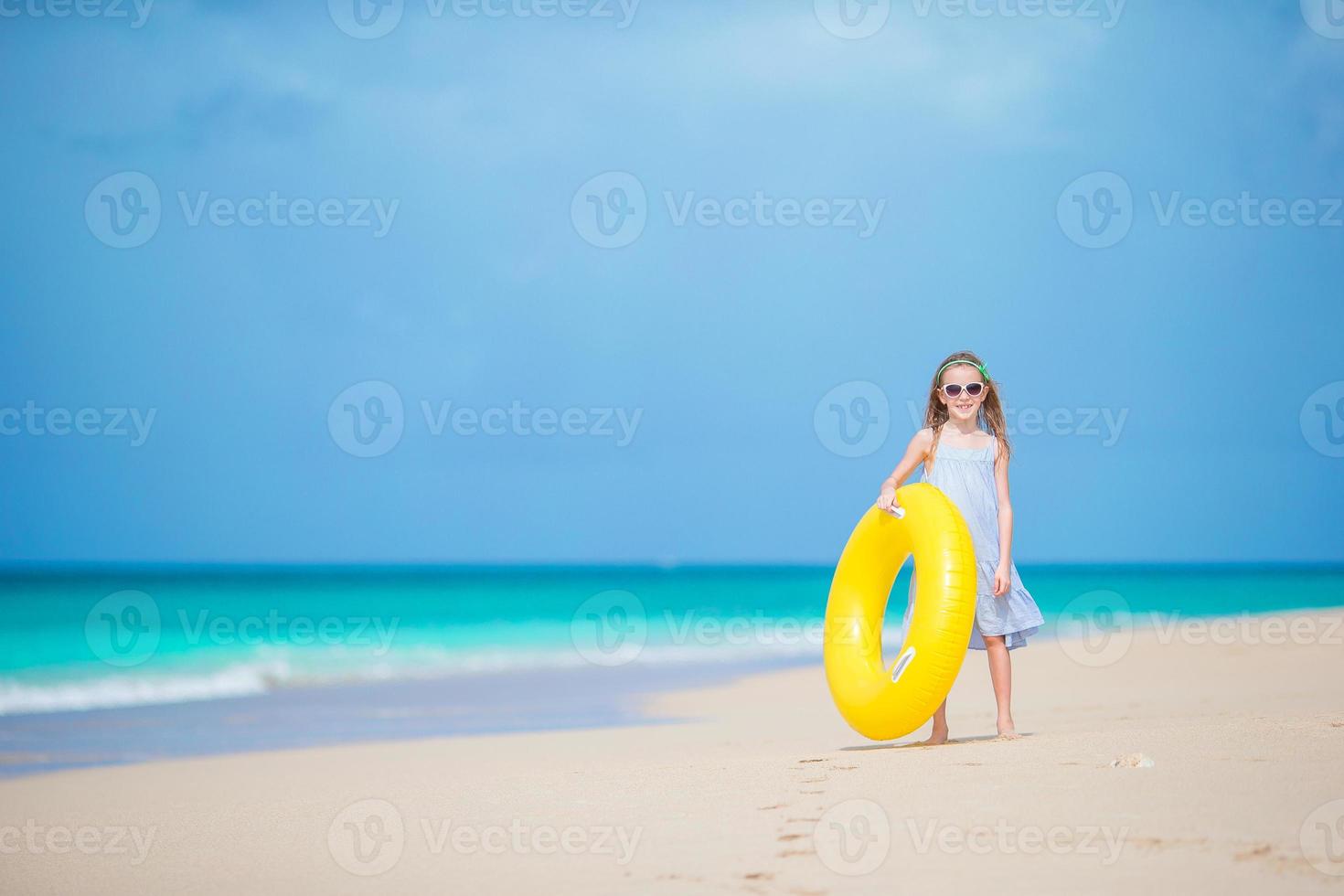 aanbiddelijk meisje met opblaasbaar rubber cirkel Aan wit strand klaar voor zwemmen foto