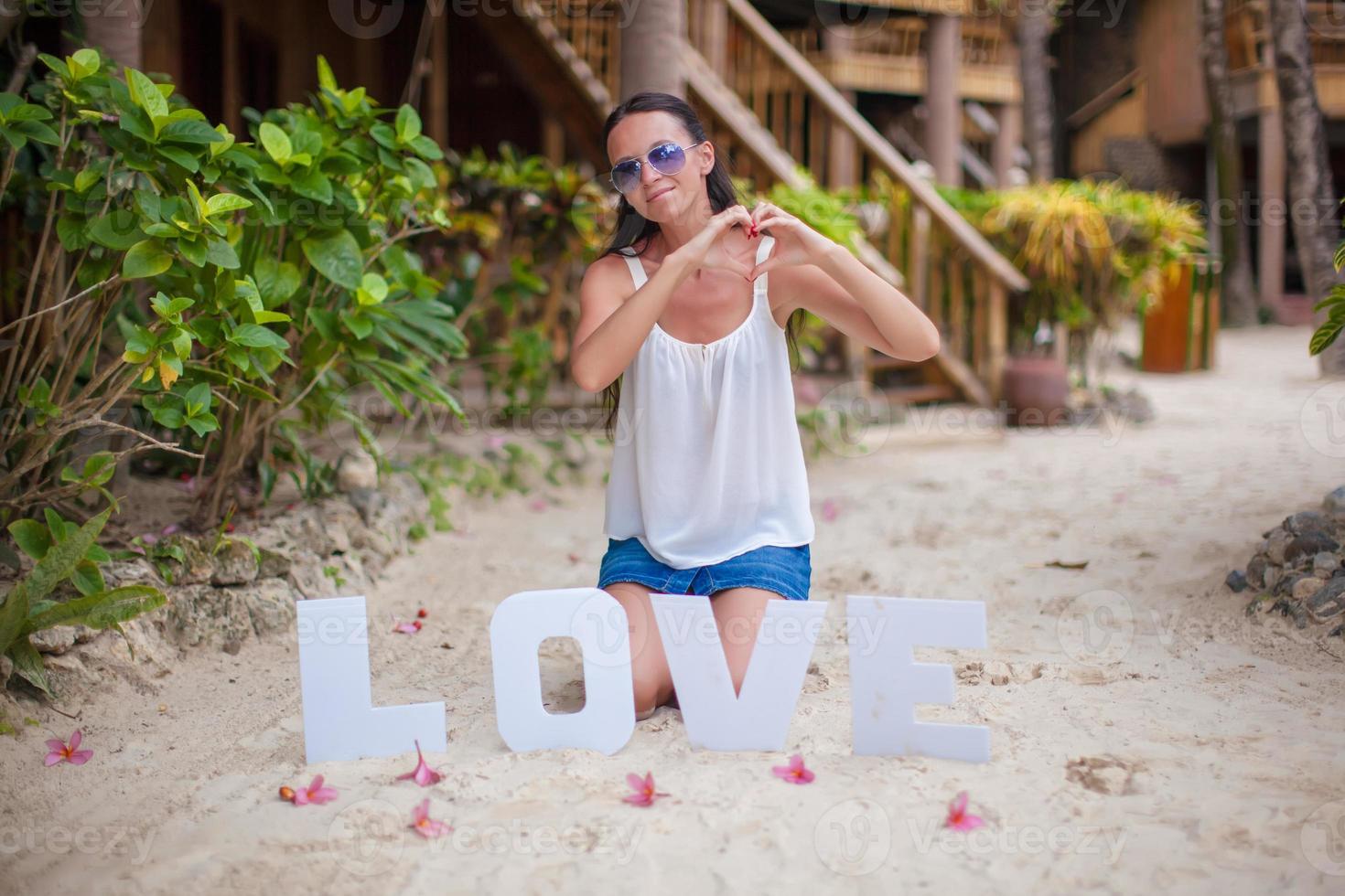 jong meisje zittend Aan zand met de woord liefde foto