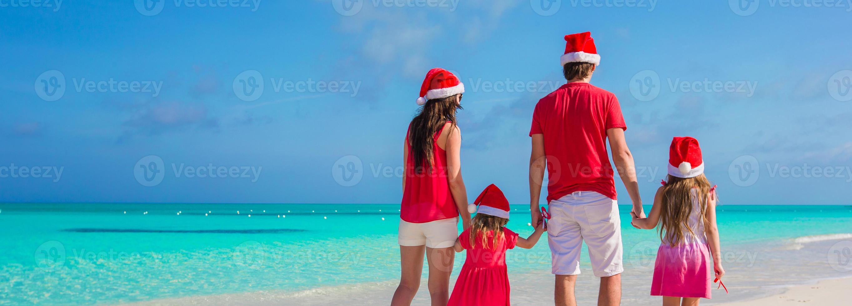 gelukkig familie van vier in Kerstmis hoeden Aan wit strand foto