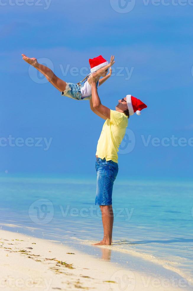 weinig meisje en gelukkig vader in de kerstman hoed gedurende strand vakantie foto