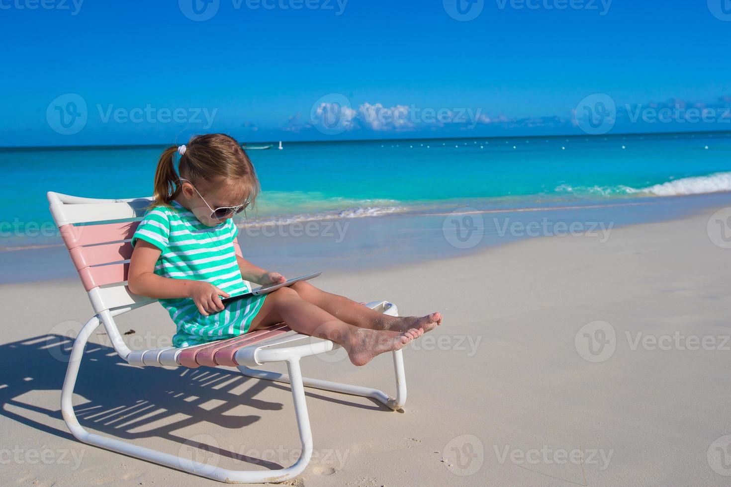 weinig meisje met laptop Aan strand gedurende zomer vakantie foto