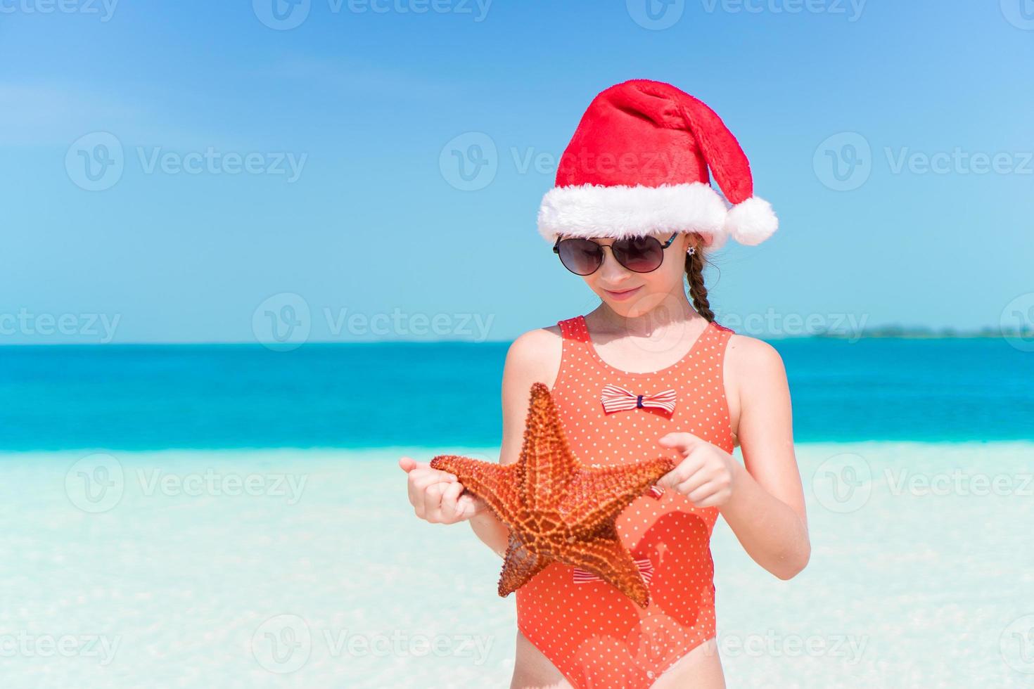 gelukkig weinig meisje in de kerstman hoed gedurende Kerstmis strand vakantie hebben een veel van pret foto