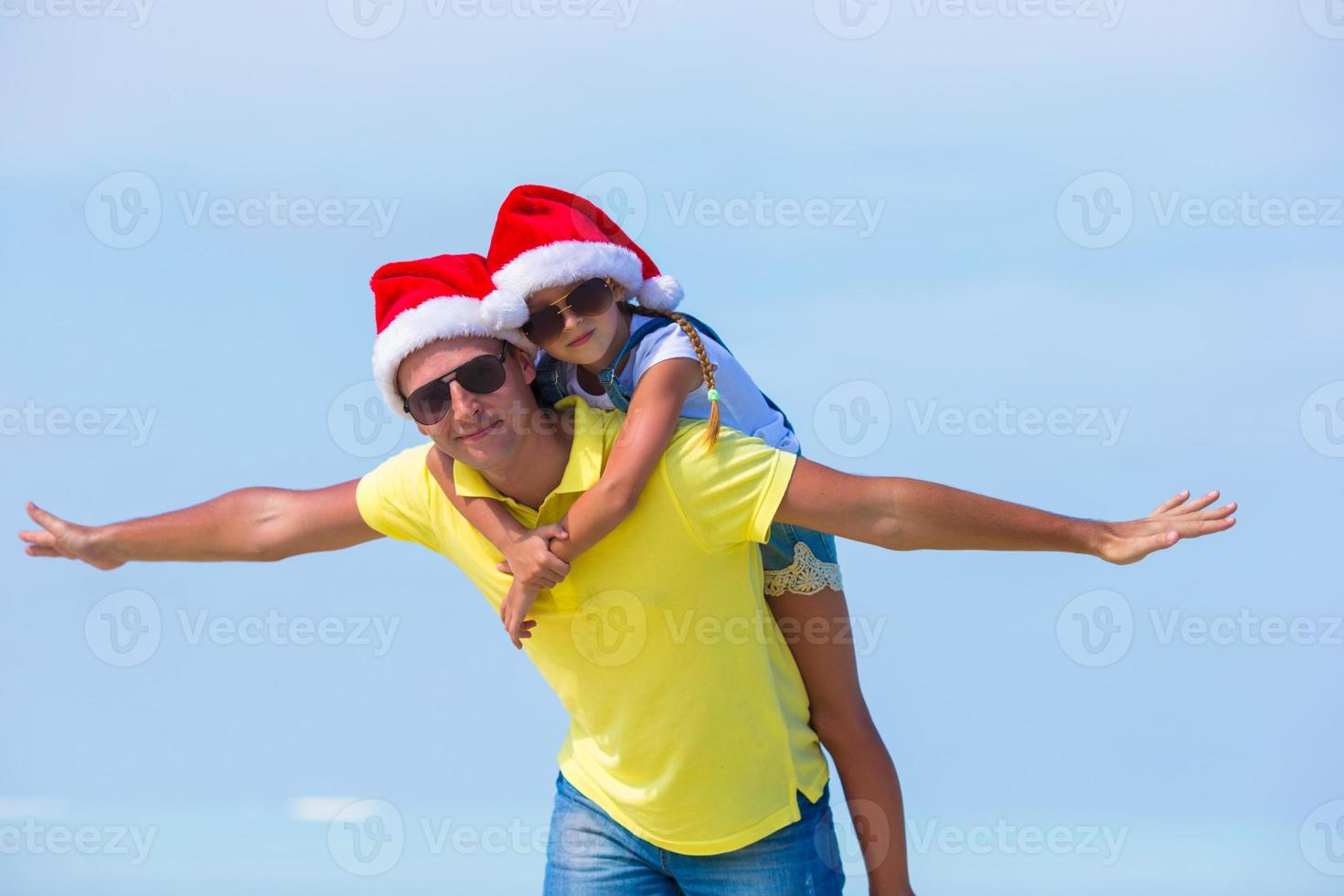 weinig meisje en gelukkig vader in de kerstman hoed gedurende strand vakantie foto