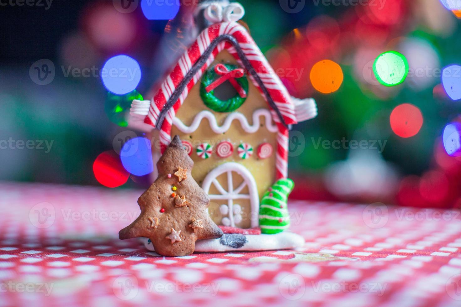 peperkoek huis versierd door zoet snoepjes Aan een achtergrond van helder Kerstmis boom met slinger foto