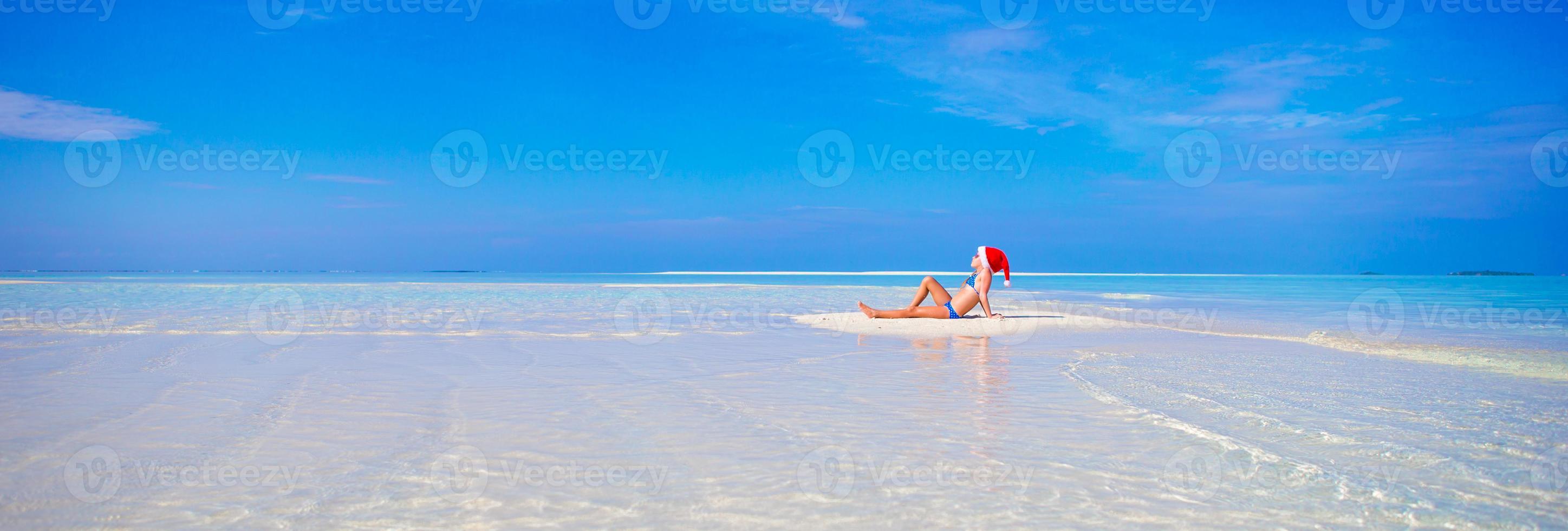 weinig meisje in de kerstman hoed Aan wit strand gedurende Kerstmis vakantie foto