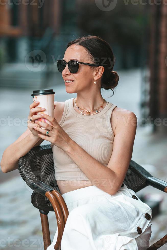 mooi vrouw hebben ontbijt Bij buitenshuis cafe. gelukkig jong stedelijk vrouw drinken koffie foto