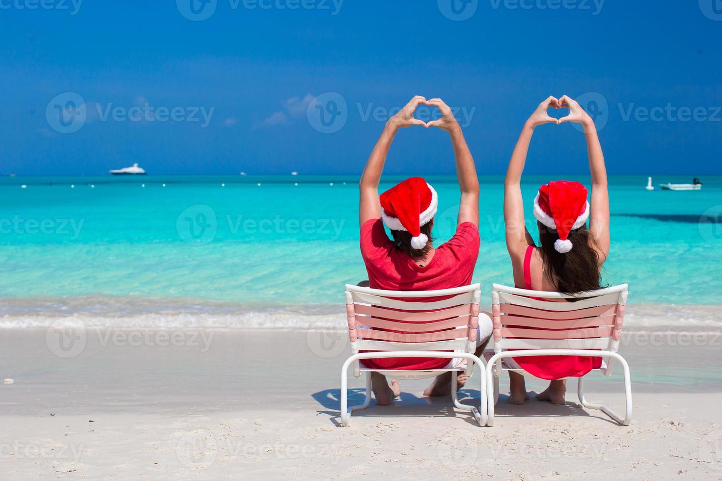 gelukkig romantisch paar in rood de kerstman hoeden Bij strand maken harten foto