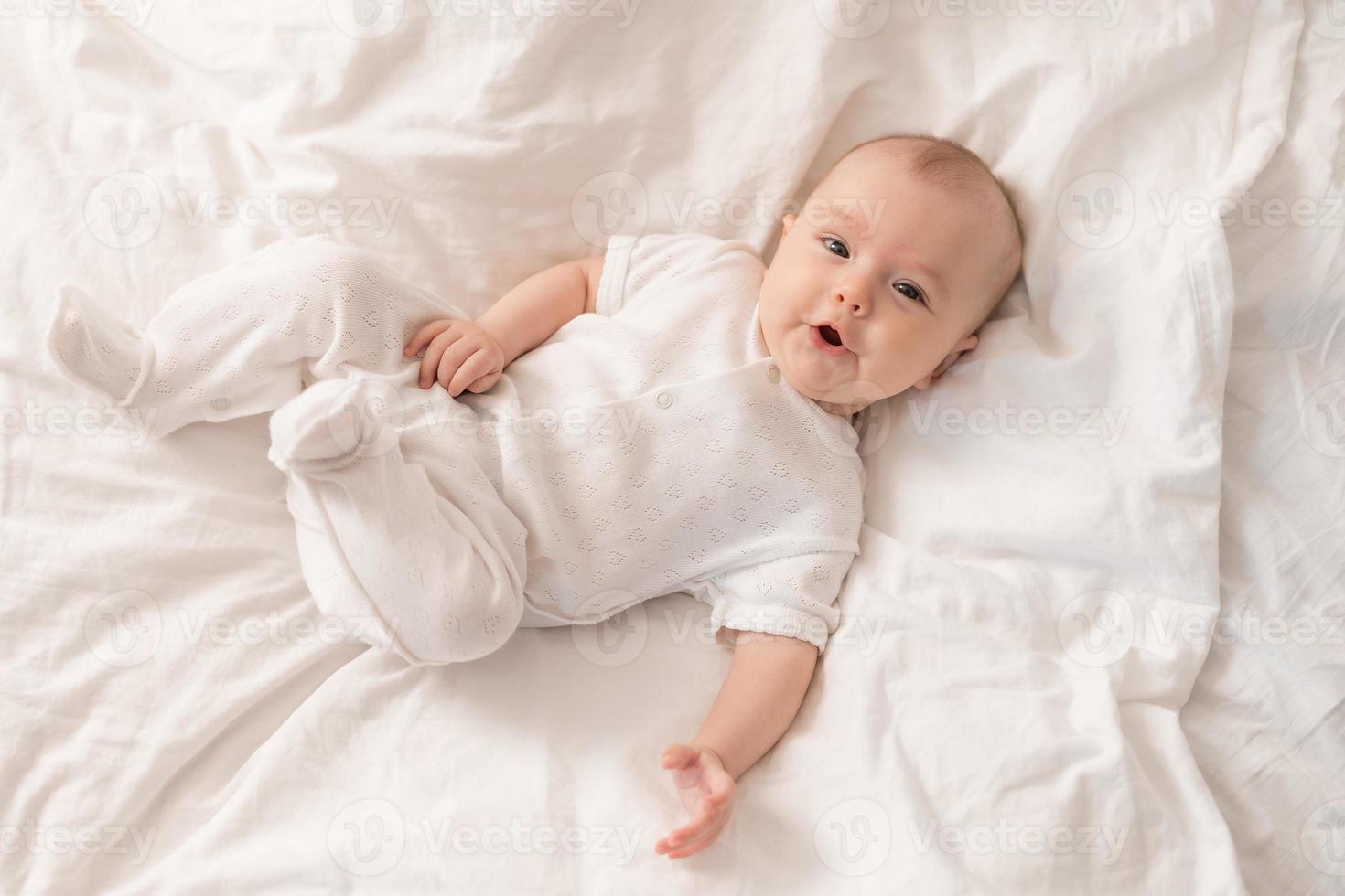 portret van een schattig baby in een wit bodysuit Aan een bed Bij huis met wit linnengoed. pasgeboren baby Bij huis, gelukkig moederschap. hoog kwaliteit foto