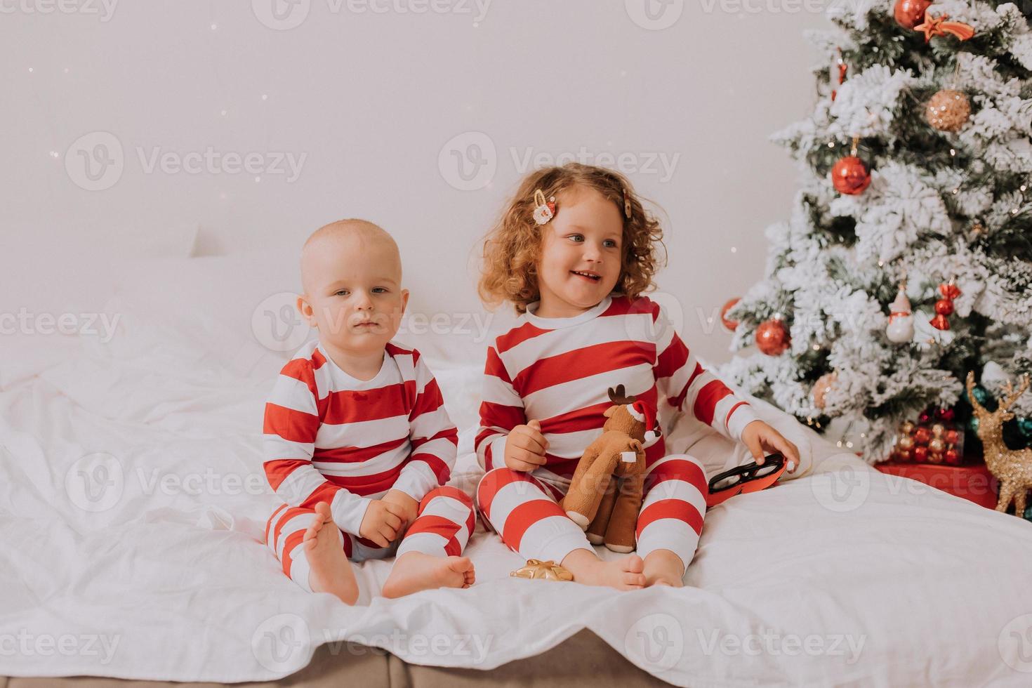 kinderen in rood en wit pyjama eten Kerstmis snoepgoed zittend in bed. broer en zus, jongen en meisje delen geschenken. Kerstmis ochtend. levensstijl. ruimte voor tekst. hoog kwaliteit foto