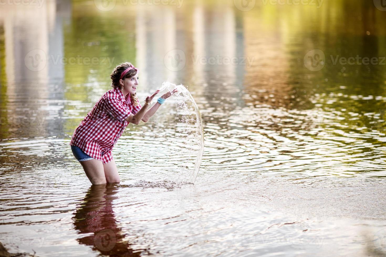 mooi jong meisje in een plaid overhemd en kort denim shorts in vastpinnen stijl blijft in water van rivier- foto