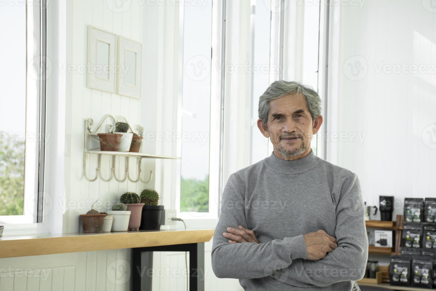 portret ouderen senior Aziatisch Mens zit in de buurt glas venster in de ochtend- naar werk van huis en controle zijn bedrijf Aan zijn laptop Aan tafel ernstig, zacht en selectief focus. foto