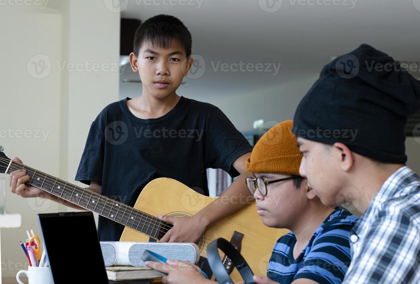 groep van jong Aziatisch tieners zittend samen binnen de kamer werken en beoefenen school- project over de muziek- onderwerpen door laptop en spelen ophouden, te, zacht en selectief focus. foto