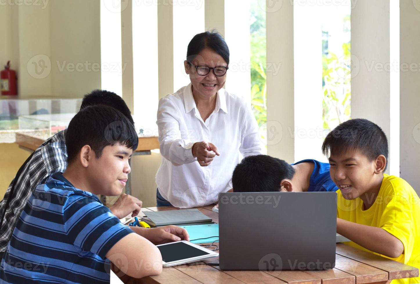 jong Aziatisch tieners en docent, ze zijn in klas, studenten aan het doen werkblad en luisteren naar haar adviezen over school- projecteren, volwassen helpt kinderen naar Doen school- project concept. foto