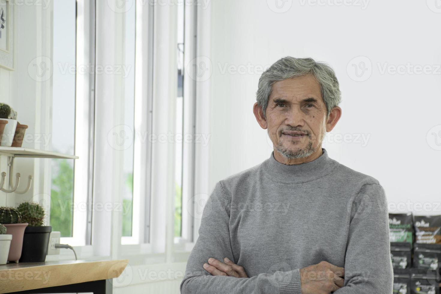 portret ouderen senior Aziatisch Mens zit in de buurt glas venster in de ochtend- naar werk van huis en controle zijn bedrijf Aan zijn laptop Aan tafel ernstig, zacht en selectief focus. foto