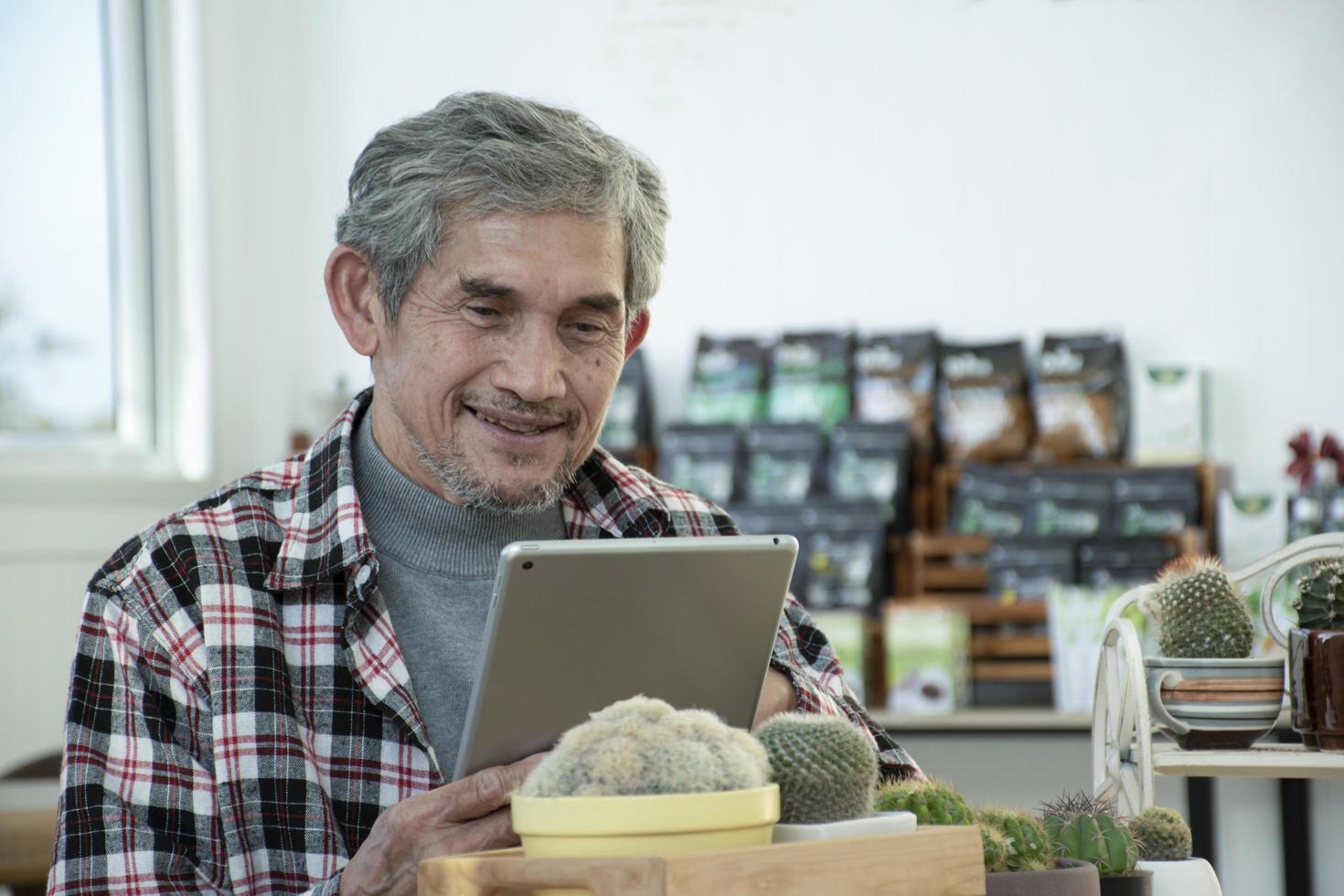 portret ouderen senior Aziatisch Mens zit in de buurt glas venster in de ochtend- naar werk van huis en controle zijn bedrijf Aan zijn laptop Aan tafel ernstig, zacht en selectief focus. foto