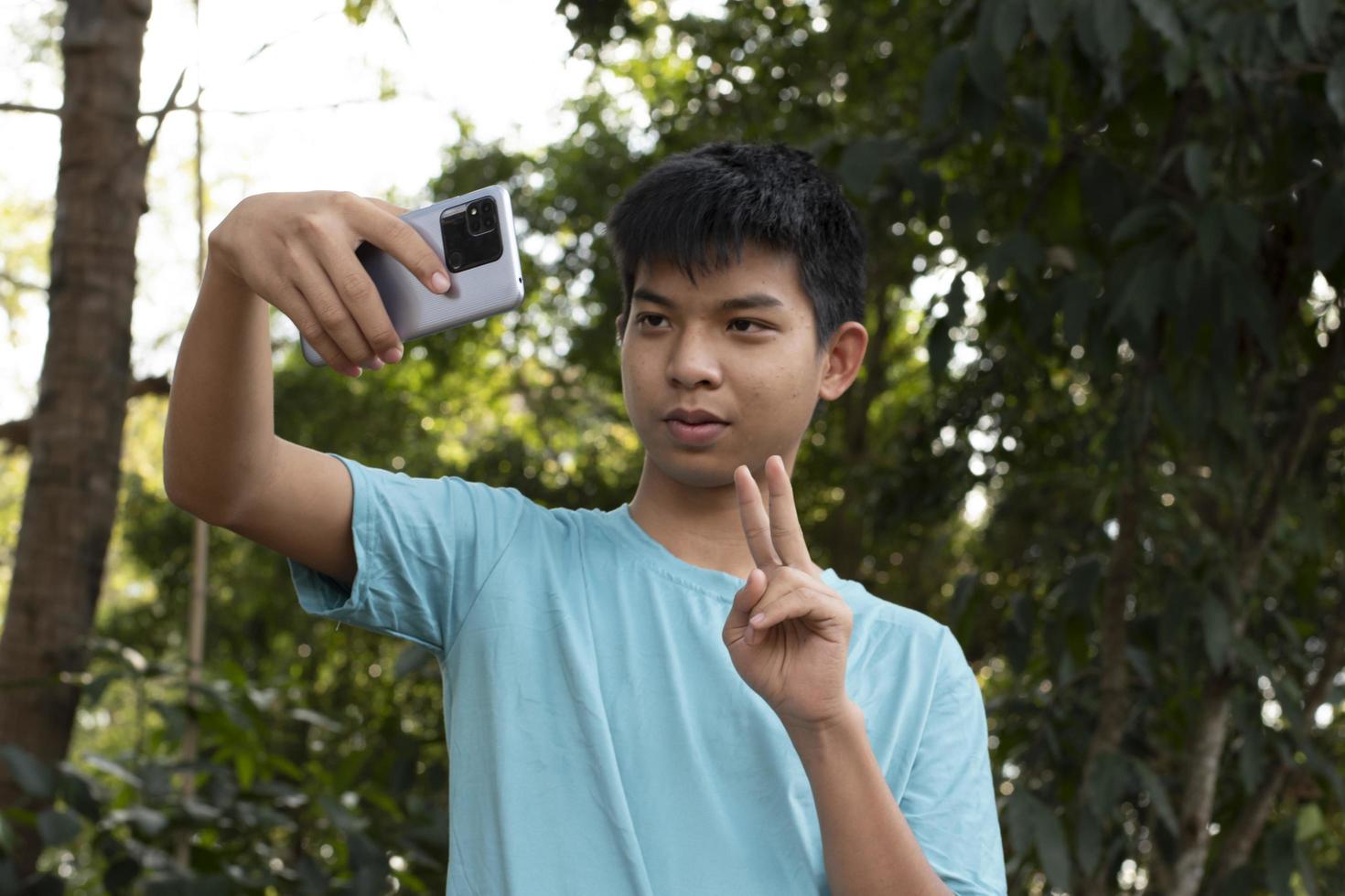 groep van jong Aziatisch tiener jongens uitgeven vrij keer in de park razen hun vingers en nemen selfie samen gelukkig, zacht en selectief focus Aan jongen in wit t-shirt, verhogen tieners concept. foto