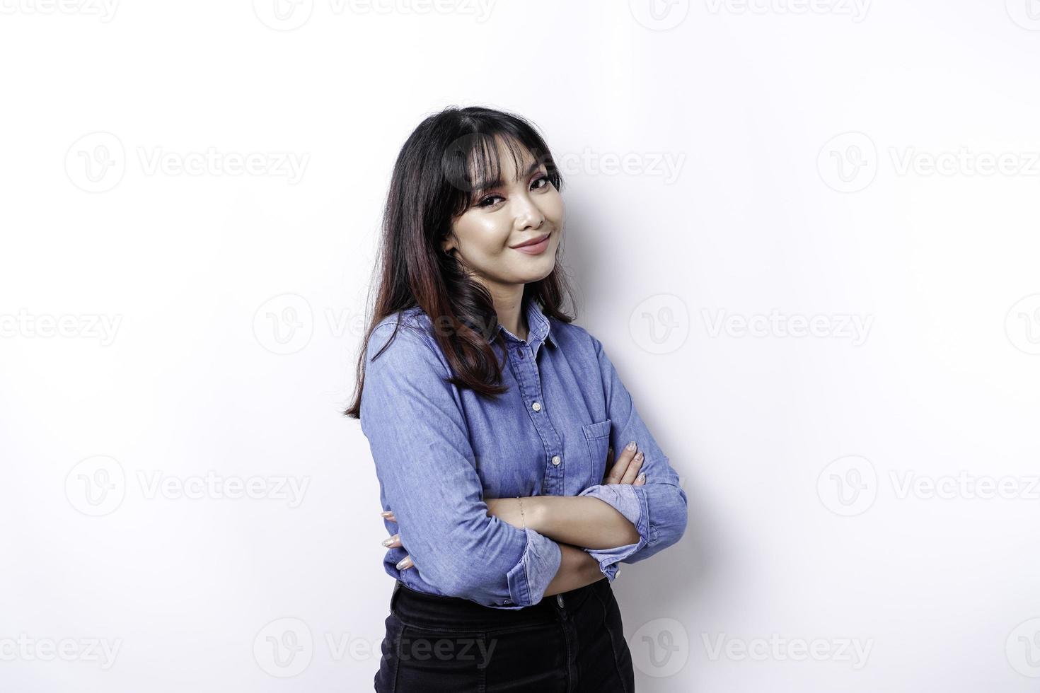 portret van een zelfverzekerd glimlachen Aziatisch vrouw vervelend blauw overhemd staand met armen gevouwen en op zoek Bij de camera geïsoleerd over- wit achtergrond foto