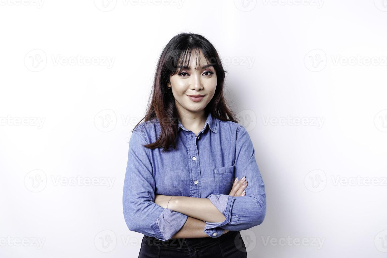 portret van een zelfverzekerd glimlachen Aziatisch vrouw vervelend blauw overhemd staand met armen gevouwen en op zoek Bij de camera geïsoleerd over- wit achtergrond foto