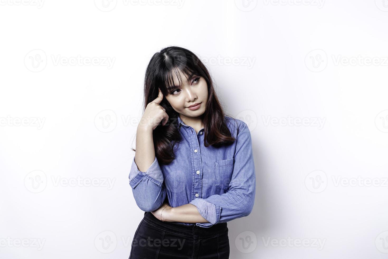 een attent jong vrouw gekleed in blauw overhemd terwijl op zoek terzijde, geïsoleerd door wit achtergrond foto