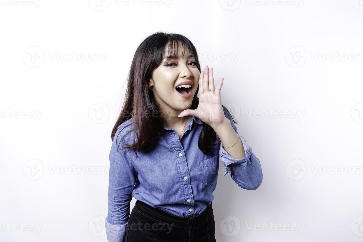 jong mooi vrouw vervelend een blauw overhemd geschreeuw en schreeuwen luid met een hand- Aan haar mond. communicatie concept. foto