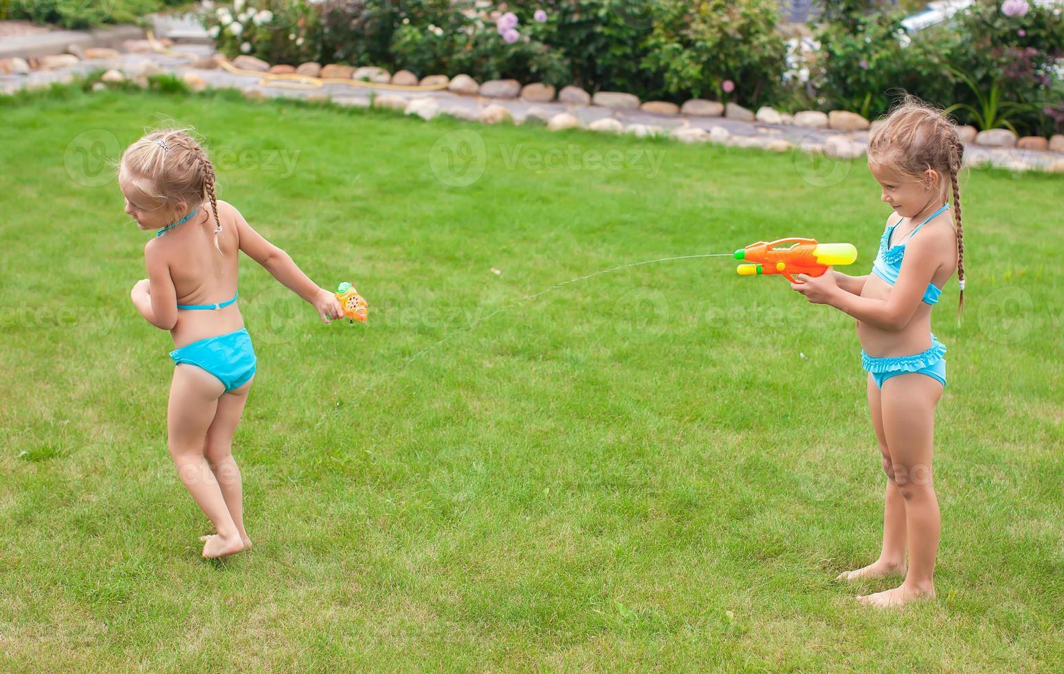 twee weinig aanbiddelijk meisjes spelen met water geweren in de werf foto