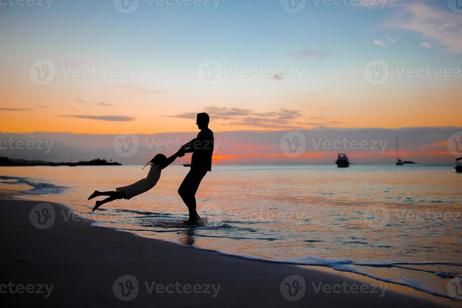 weinig meisje en gelukkig vader silhouet in de zonsondergang Bij de strand foto
