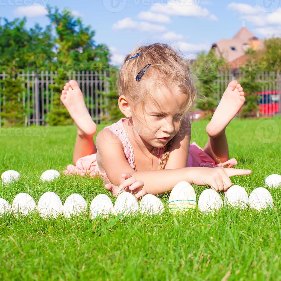 weinig gelukkig en grappig meisje spelen met Pasen eieren Aan groen gras foto