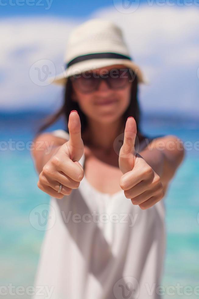 jong aanbiddelijk vrouw tonen duimen omhoog Aan wit strand foto