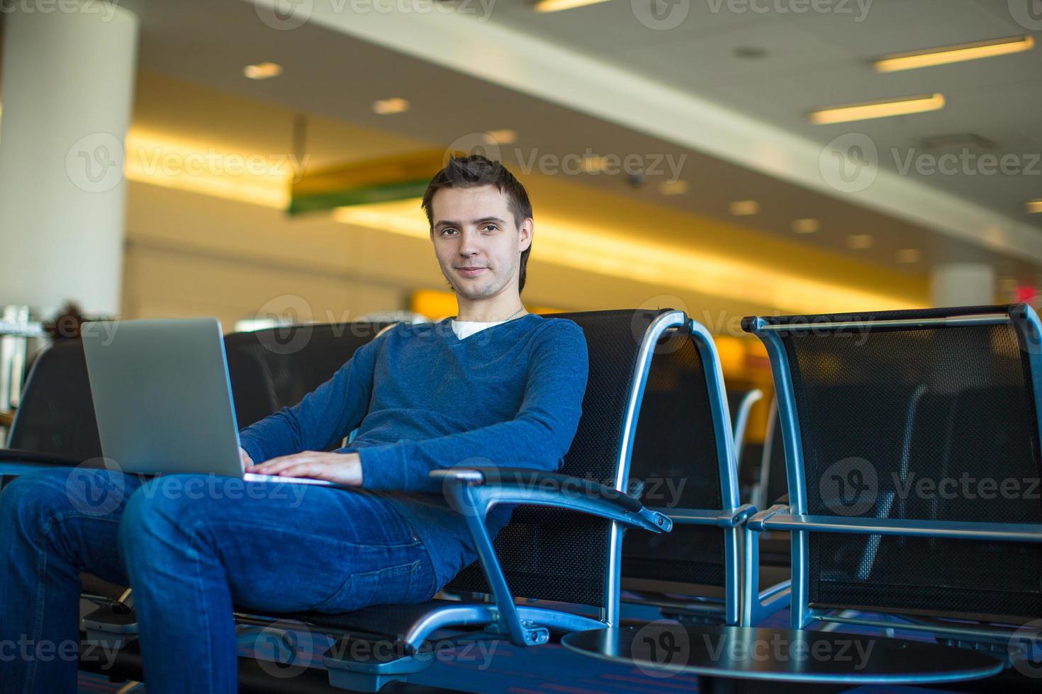 jonge man met een laptop op de luchthaven tijdens het wachten op zijn vlucht foto