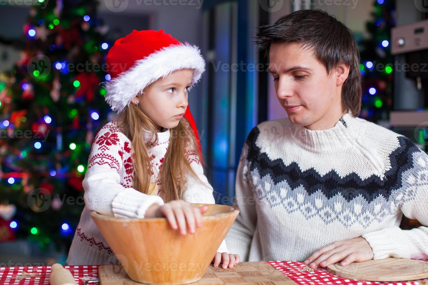 jong vader met weinig dochter in de kerstman hoed bakken peperkoek koekjes foto