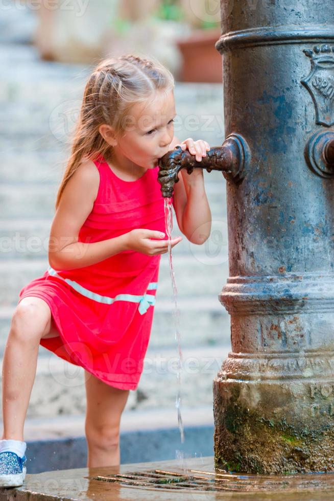 weinig aanbiddelijk meisje drinken water van de kraan buiten Bij heet zomer dag in Rome, Italië foto
