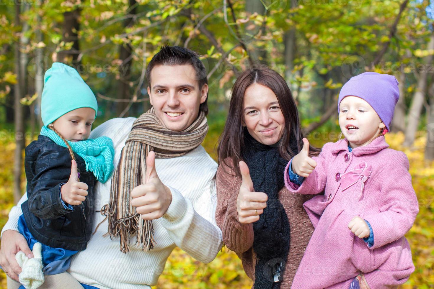 familie van vier genieten van herfst vakantie en tonen een duimen omhoog foto