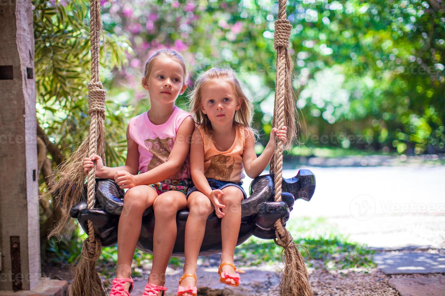 weinig meisjes swinging in een knus lief gebloeid binnenplaats foto